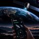 A hand holds a smartphone displaying the Starlink Mobile app interface showing a strong “Connected – Direct to Cell” signal, with a Starlink satellite beaming connectivity signals down to Earth from orbit. The background features the planet’s night side glowing with city lights against the curve of the atmosphere, set above a scenic twilight landscape.
